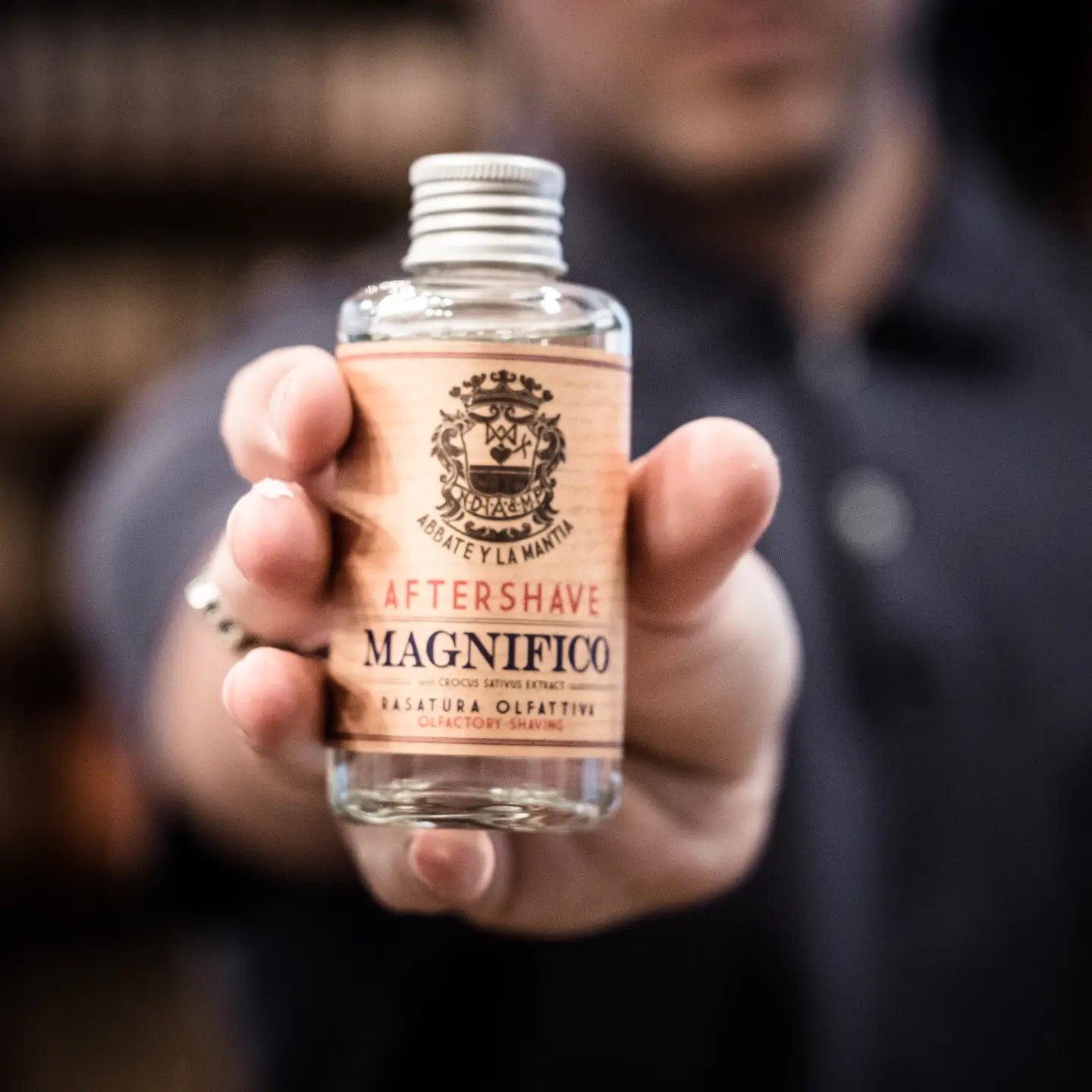 Hand holding a bottle of after-shave labeled 'Magnifico' with a blurred background