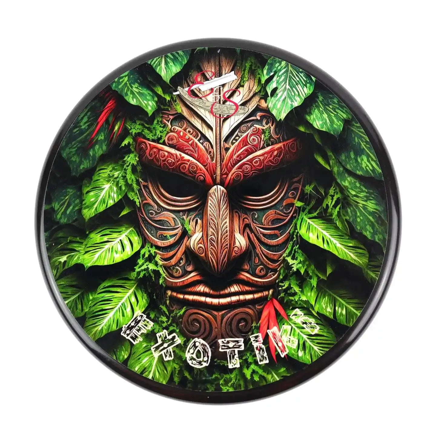Decorative wall clock with a tiki mask design on a green leafy background