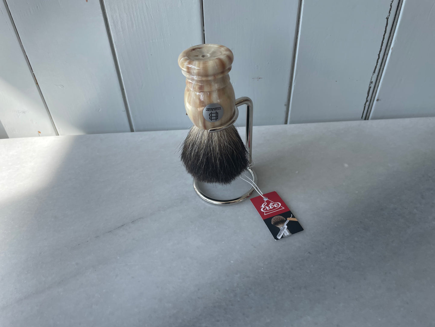 Shaving brush with a wooden handle and black bristles on a white surface, featuring a brand tag.