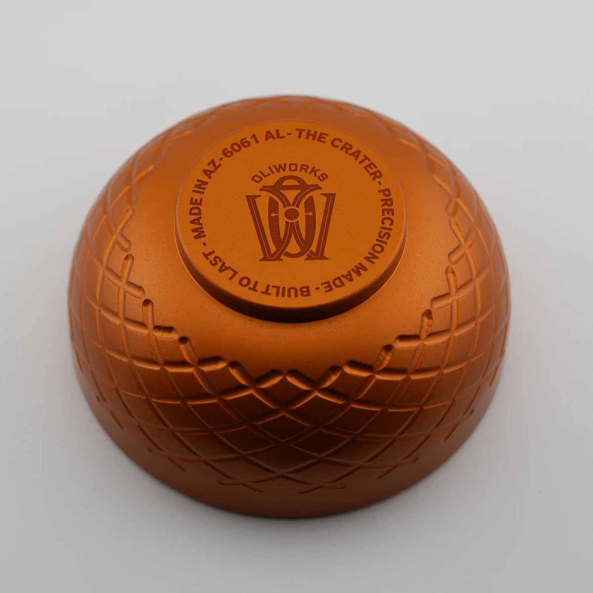 Bronze-colored metal ball with engraved text and logo on a light gray background