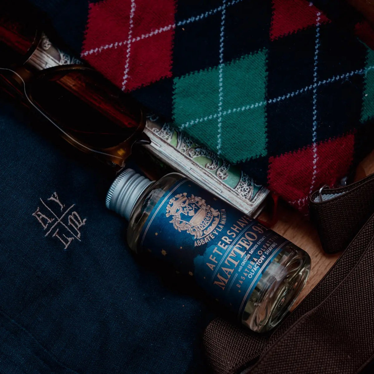 Aftershave bottle with a plaid fabric and sunglasses in the background