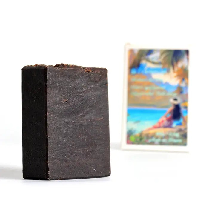 Bar of dark soap on a white background with a blurred beach scene in the background