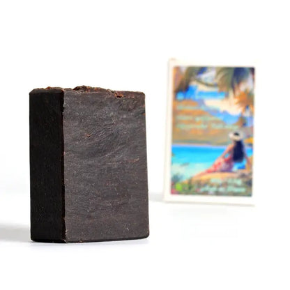 Bar of dark soap on a white background with a blurred beach scene in the background