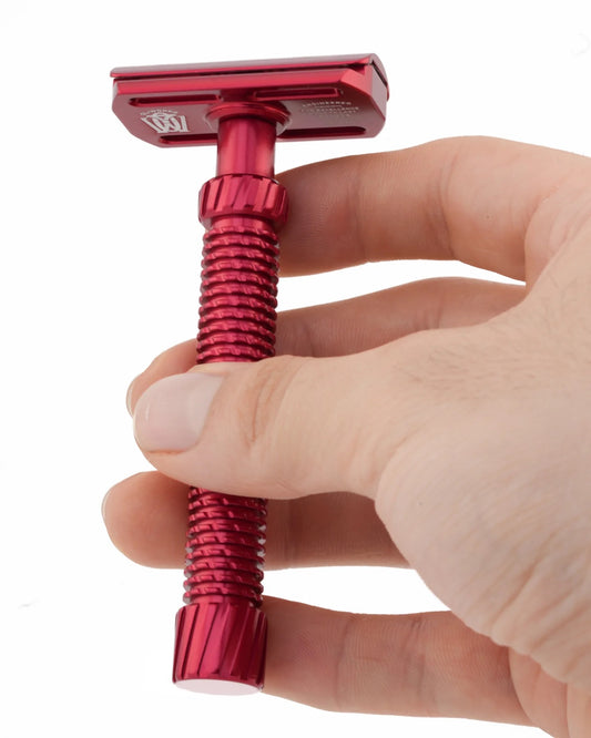 Red safety razor held by a hand on a white background