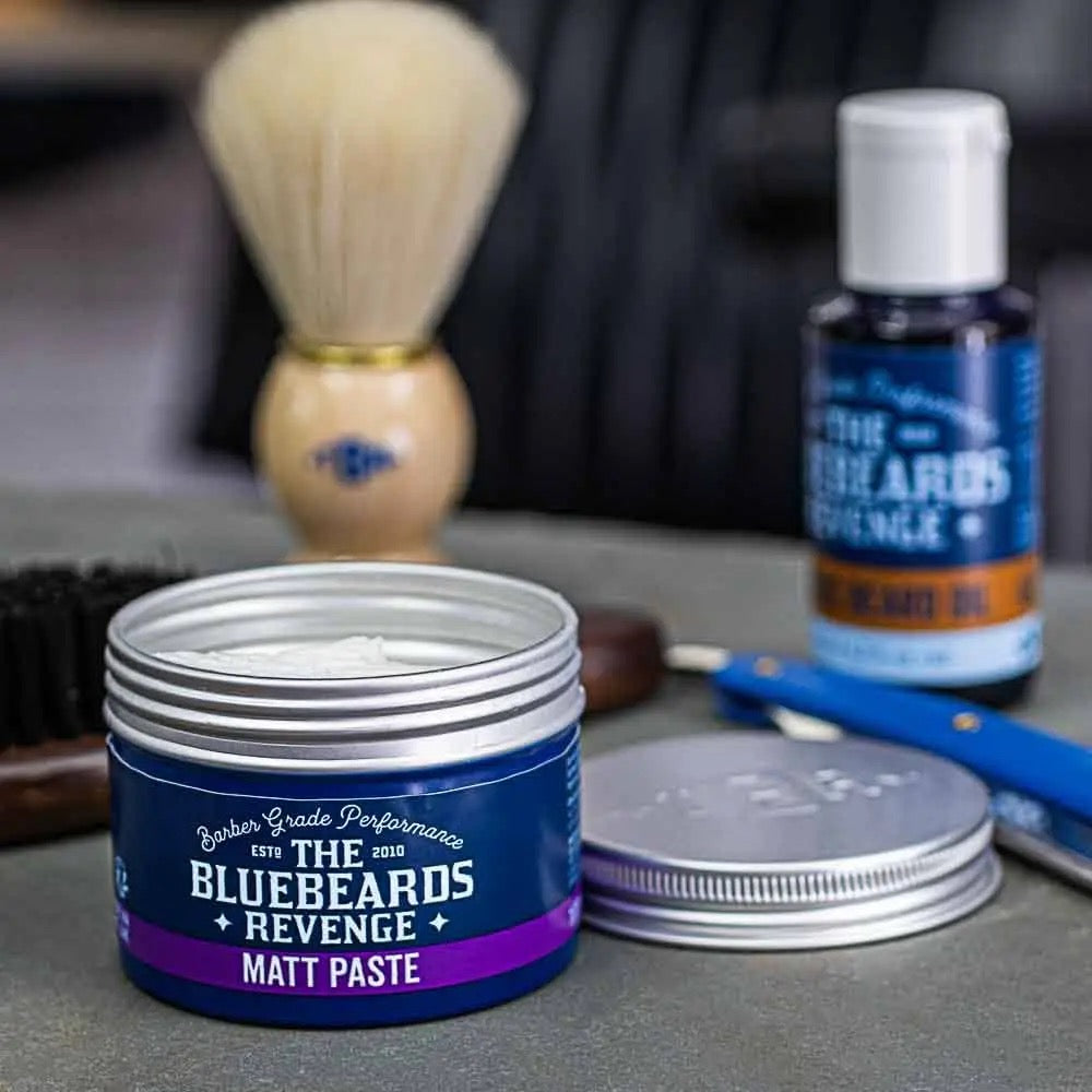 Bluebeards Revenge Matt Paste jar with shaving brush and other products on a gray surface
